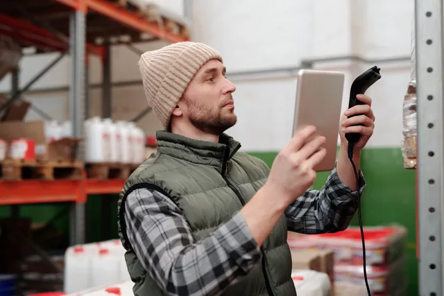 Man in beanie and vest using a scanner in a warehouse for inventory control. Workflow monitoring and observability